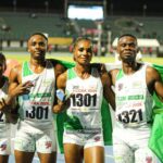 Four Nigerian track athletes pose together after a race holding a green and white Nigerian flag on a stadium track  trybalnews