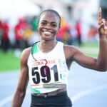 Smiling female long distance runner on a track wearing bib 591 with Accra 2026 raising one finger in victory  trybalnews