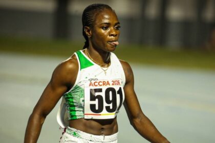 Female sprinter in a white and green athletic outfit with bib 'ACCRA 2026' and number 591, walking on a track after a race.