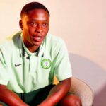 Young man in a mint green polo with a Nigeria Football Federation crest sitting in a beige armchair in a softly lit room  trybalnews
