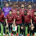 Soccer team in red and black striped jerseys posing for a group photo on the field goalkeeper in purple stands behind them  trybalnews