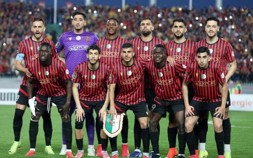 Soccer team in red and black striped jerseys posing for a group photo on the field goalkeeper in purple stands behind them  trybalnews