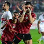 Two soccer players in red and black striped jerseys celebrate on the field one making a playful glasses gesture with his hands around his eyes  trybalnews