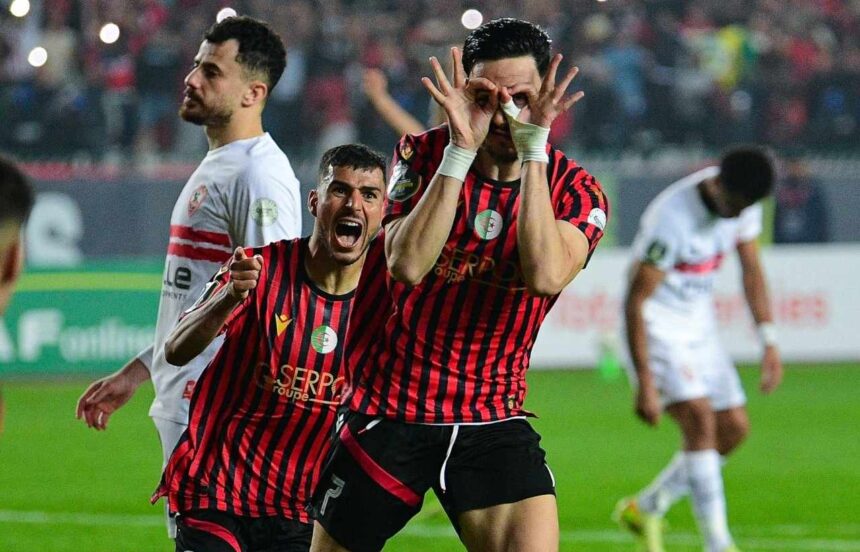 Two soccer players in red and black striped jerseys celebrate on the field one making a playful glasses gesture with his hands around his eyes  trybalnews