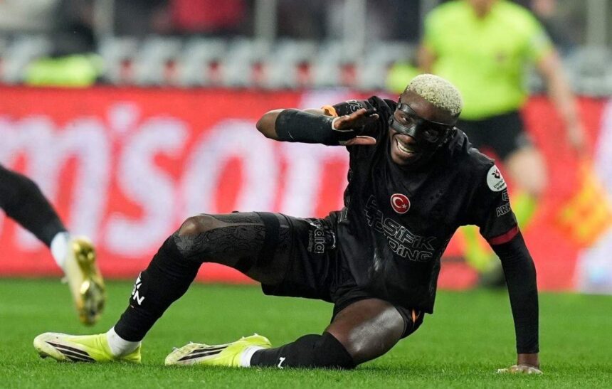 Soccer player in black kit sliding on grass reaching with one hand during a match smiling  trybalnews