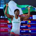 Nigerian athlete lifts the green white green flag in celebration on a podium or stage wearing Nigeria kit with NIGERIA visible  trybalnews