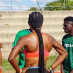 Athletes on a track field chat central figure is a woman with braided hair seen from behind  trybalnews