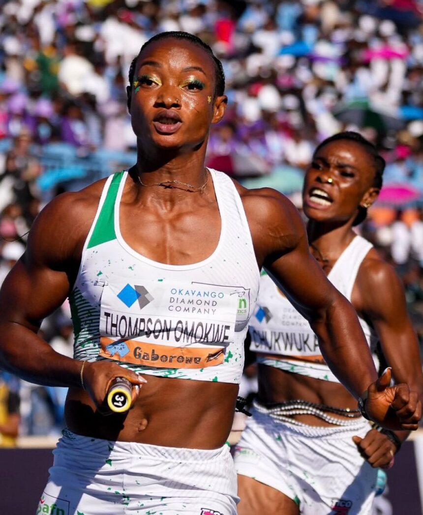 Two female sprinters race toward the finish in a crowded stadium foreground runner in a white and green kit holds a baton as she moves forward  trybalnews