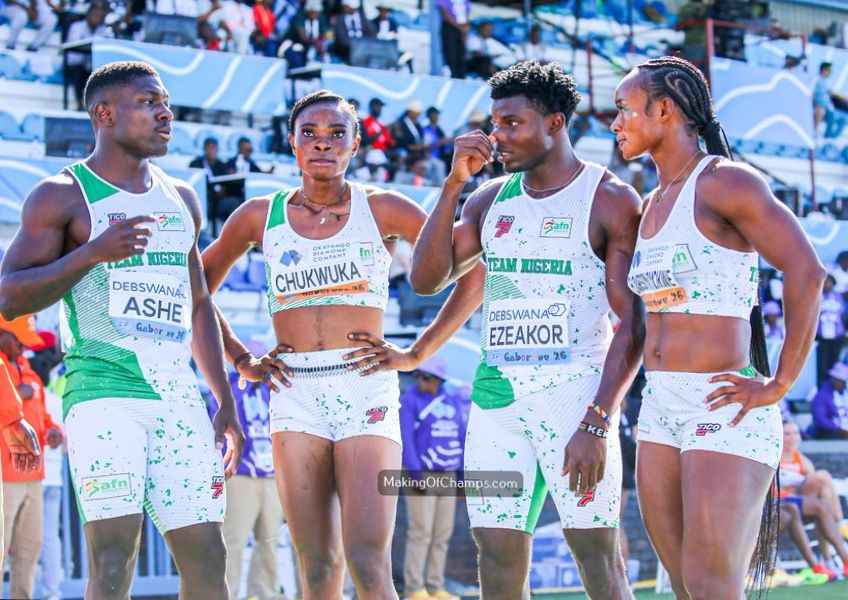 WhatsApp Image 20260502 at 180936 Trybal News Four athletes in white and green track uniforms stand together on a stadium track their hands on hips or near their faces with race bibs visible on their chests names like CHUKNUKA and EZEAKOR and a cheering crowd in the background trybalnews