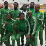 Group of athletes in matching green tracksuits posing for a team photo in an indoor facility some crouching in front and others standing behind The uniforms feature Nigeria flag patches on the jackets  trybalnews