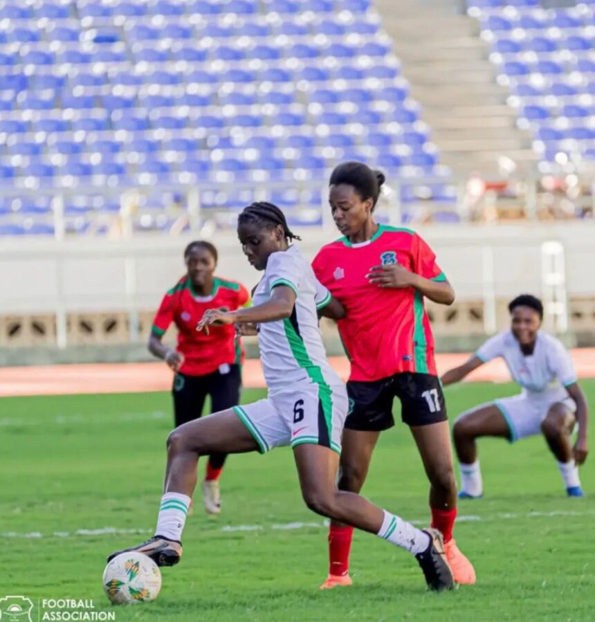 Soccer match in progress with players in white and red uniforms contesting the ball on a green field blue stadium seats in the background  trybalnews