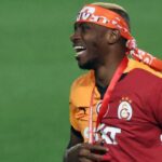 Soccer player in a red orange Galatasaray kit with a headband smiling on the field during a celebration  trybalnews