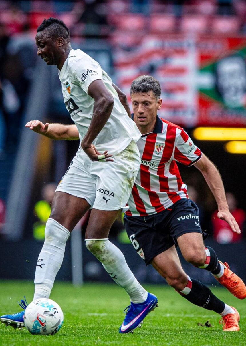 Two soccer players contest a ball on the field a white kit player shields the ball while a red and white striped opponent closes in  trybalnews