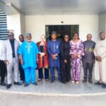 Group of twelve adults standing in a line outside a modern building entrance wearing colorful traditional and business attire with smiles  trybalnews