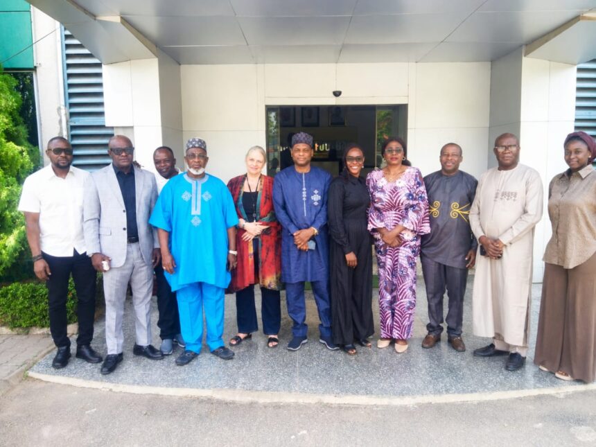 Group of twelve adults standing in a line outside a modern building entrance wearing colorful traditional and business attire with smiles  trybalnews