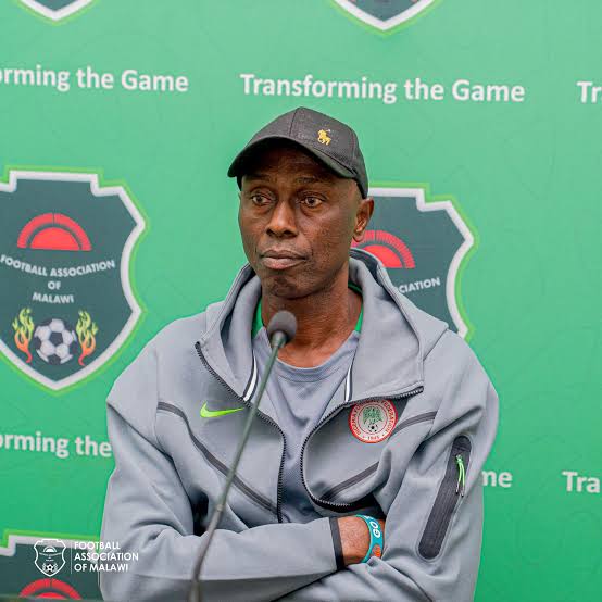 Man wearing a gray jacket and cap sits at a microphone at a Malawi Football Association press conference with a green backdrop  trybalnews