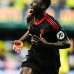 Soccer player in a black jersey with red trim celebrates a goal tongue out running on the field with a blurred stadium background  trybalnews