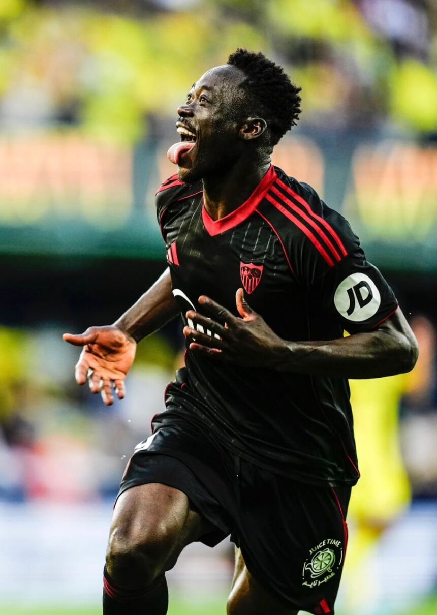 Soccer player in a black jersey with red trim celebrates a goal tongue out running on the field with a blurred stadium background  trybalnews