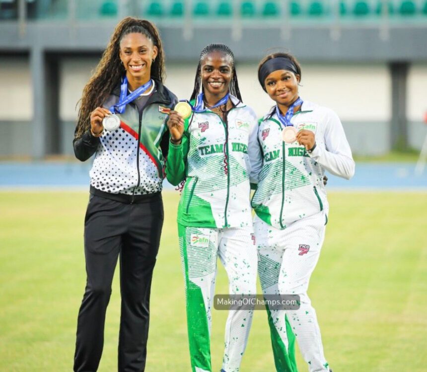 Three female athletes stand together on a track field smiling and showing their medals in team uniforms  trybalnews