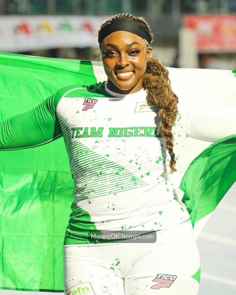 Female Nigerian athlete smiles while holding a green and white flag wearing a TEAM NIGERIA jersey  trybalnews