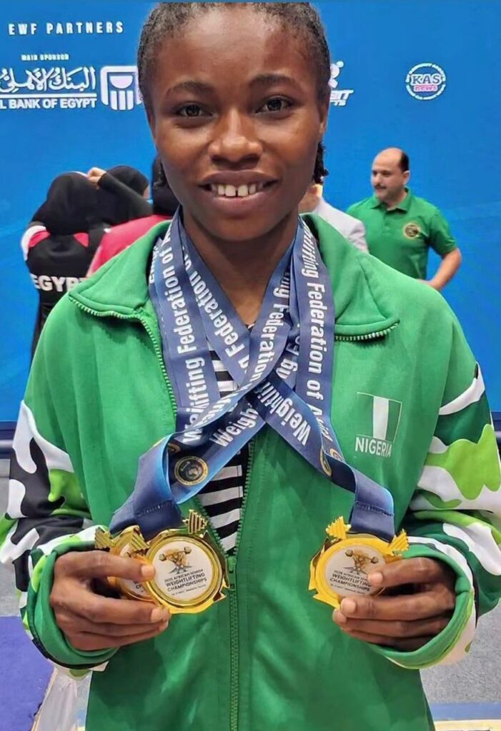 Young Nigerian athlete smiles wearing a green jacket and multiple weightlifting medals at a sports event  trybalnews