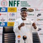 Nigerian football official in white attire holding a sign that says Enyimba intl FC at a press conference with NFF backdrop behind him  trybalnews