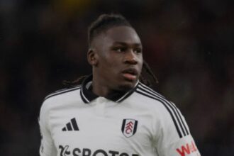 Footballer in a white Fulham kit sprinting during a match, with SBOTOP sponsor logo visible on the front.