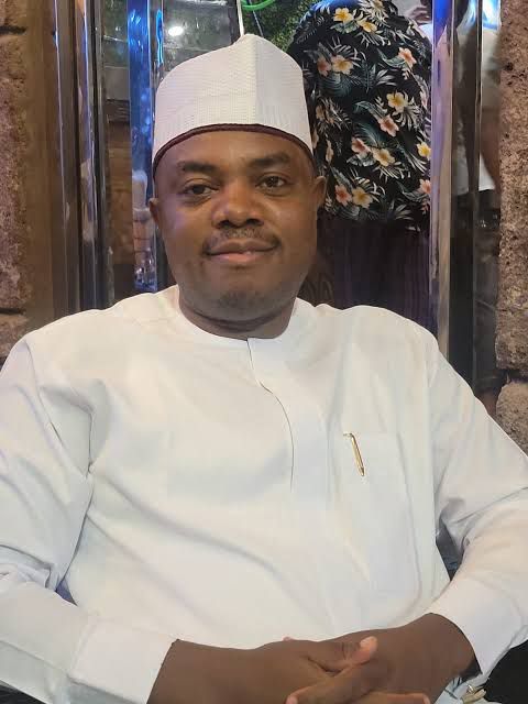 Man wearing a white traditional outfit and cap seated and smiling at the camera in a dining setting  trybalnews