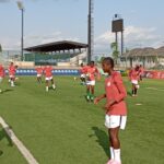 Soccer training on a sunny field with female players in red jerseys and white shorts handling balls statuesque on green turf  trybalnews