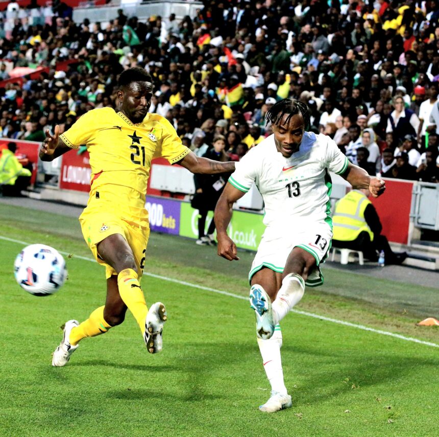 Two soccer players in yellow and white kits chase a ball on a green pitch with a crowded stadium in the background mid action  trybalnews