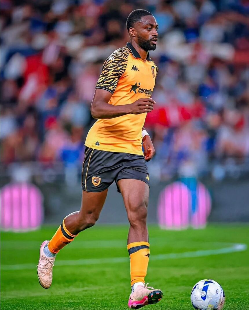 Soccer player in an orange jersey and black shorts running with the ball on a green pitch stadium crowd in the background  trybalnews