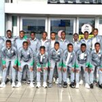 Group of 18 young athletes in matching gray tracksuits with green accents pose for a team photo outside a building  trybalnews