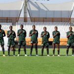 Soccer team lined up on a grassy field with hands over their hearts wearing green uniforms in a stadium   trybalnews
