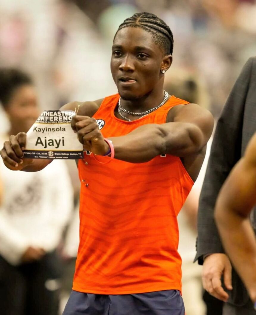 Male sprinter in an orange sleeveless top holds up a race bib reading Kayinsola Ajayi during a track meet  trybalnews