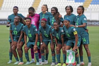 Nigeria women's national football team posing for a group photo on the soccer field in teal uniforms.
