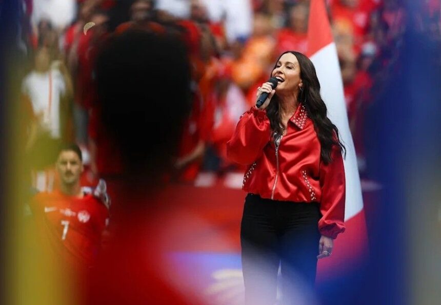 Female singer wearing a bright red jacket performs into a handheld microphone on a crowded stage  trybalnews