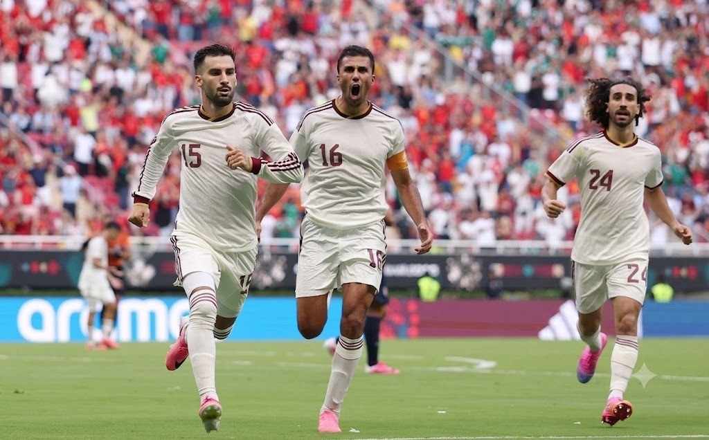 Alex Baena Trybal News Spain midfielder Alex Baena wearing a white away kit with maroon number 15 runs with a focused expression after scoring He is joined by teammates 16 who is shouting with his mouth open and 24 with curly hair on the right All three wear white shirts with maroon trim and pink cleats 2026 FIFA World Cup Group H match between Uruguay and Spain on June 26 2026 at Guadalajara Stadium in Zapopan Mexico A packed stadium with red seats and a blurred crowd is in the background trybalnews