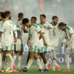 Soccer players in white and green kits huddle together on the field after a match with colorful cleats and a smoky stadium in the background  trybalnews