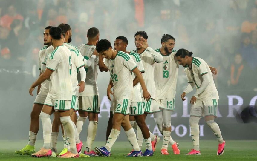 Soccer players in white and green kits huddle together on the field after a match with colorful cleats and a smoky stadium in the background  trybalnews