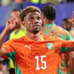 Amad Diallo in an orange jersey with the number 15 raising both arms and pointing upward with his index fingers in celebration  trybalnews