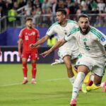 Amine Gouiri in Algerias white 9 jersey with green stripes runs forward with mouth open and arms outstretched in celebration He wears white shorts socks with FAF and pink football boots Behind him an Algeria teammate in the same kit runs and shouts with his right fist clenched Two Jordan players in red 5 and 11 jerseys stand dejected in the background The match is Jordan vs Algeria at San Francisco Bay Area Stadium FIFA World Cup 2026 Group J June 22 2026 Santa Clara California A packed stadium crowd is blurred behind a blue advertising board  trybalnews
