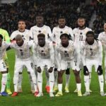 Ghana football team in white kits with star crests posing for a group photo on the pitch before a match with fans in the stands behind them  trybalnews