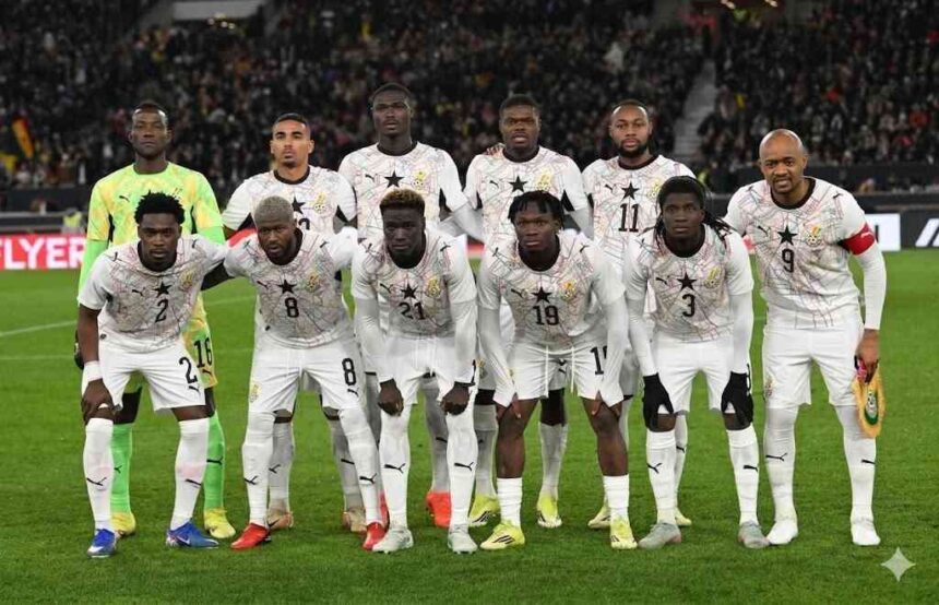 Ghana football team in white kits with star crests posing for a group photo on the pitch before a match with fans in the stands behind them  trybalnews