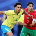 Two soccer players one in yellow Brazil kit and one in red Morocco kit chase the ball in a crowded match  trybalnews
