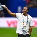 Sports official on a field smiling and waving a folded shirt above his head  trybalnews