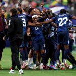 Cabo Verde players in dark blue kits with white numbers celebrate on the pitch after a 0 0 draw Player 11 wearing a white headband smiles and is hugged in the center with teammate 22 MOREIRA to his right and 9 MENDES behind him A staff member in a maroon shirt raises a blue gloved fist on the left and another staff member holds a camera on the right 2026 FIFA World Cup Group H match between Cabo Verde and Saudi Arabia on June 26 2026 at Houston Stadium in Houston Texas A blurred crowd fills the stadium background  trybalnews