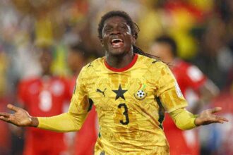 Ghana national team player in a yellow kit celebrating with arms outstretched on the field.