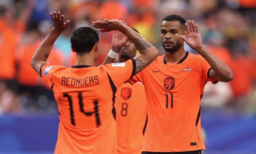 Netherlands players Cody Gakpo wearing orange jersey number 11 and Tijjani Reijnders wearing orange jersey number 14 celebrate together on the pitch Gakpo faces the camera with both hands raised while Reijnders has his back to camera with arms up high Both wear orange Netherlands kits with the Dutch crest A third teammate in jersey number 8 is blurred in the background Fans in orange fill the stadium stands behind them Match was FIFA World Cup 2026 Group F Netherlands vs Sweden at Houston Stadium Houston Texas on June 20 2026  trybalnews