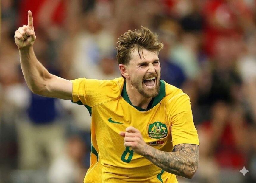 Australian soccer player in a yellow jersey celebrates a goal fist raised and shouting  trybalnews
