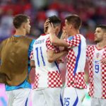 Croatia midfielder Mario Pasalic and forward Andrej Kramaric wearing red and white checkered 9 jersey celebrate by hugging forward Ante Budimir in 11 jersey after a win Fourth Croatia player in checkered jersey visible on right Blurred crowd in red and pink LED advertising board in background during 2026 World Cup Group L match between Panama and Croatia at Toronto Stadium Toronto on June 23 2026  trybalnews